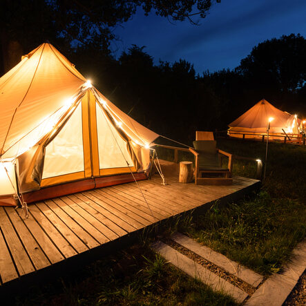 Glamping tents with burning torches, lamps and wooden chairs at glamping, forest around, night